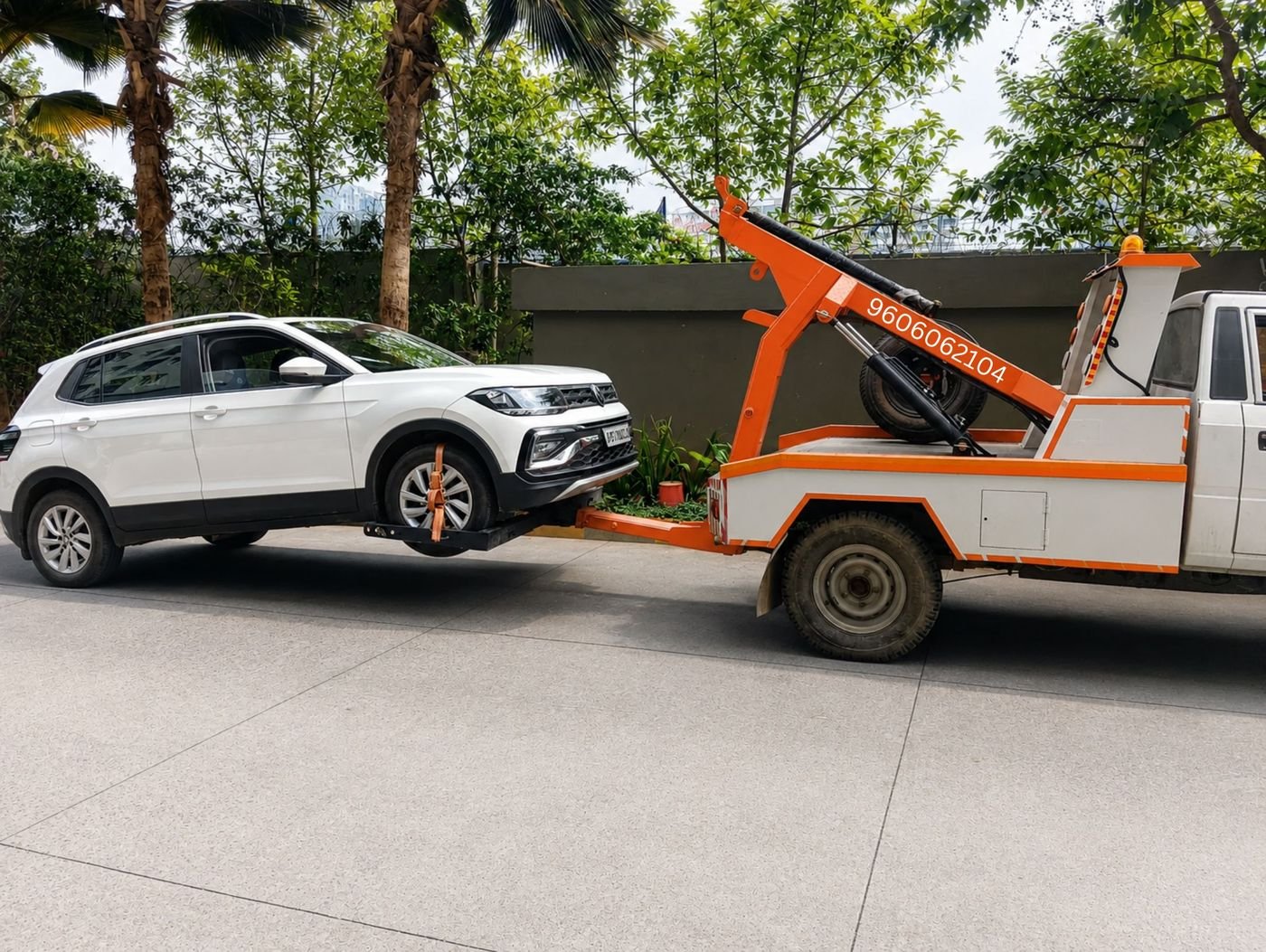 Ganesh Towing Service Bangalore orange tow truck lifting a white SUV, phone number 9606062104 on the boom