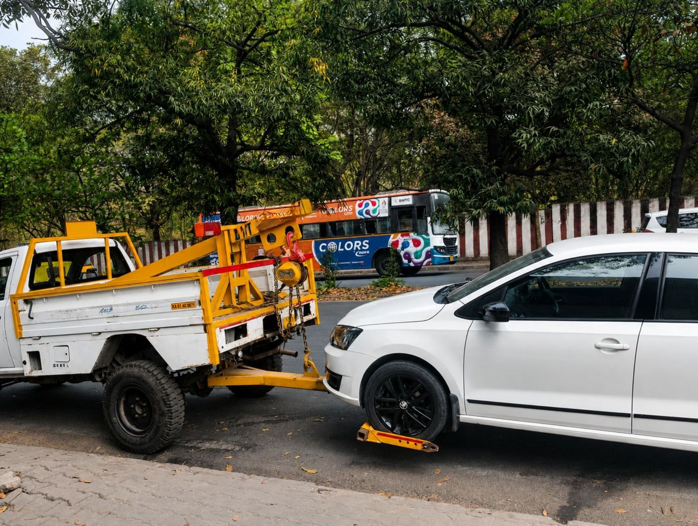 Yellow wheel lift tow truck attached to a white sedan for emergency vehicle towing in Bangalore